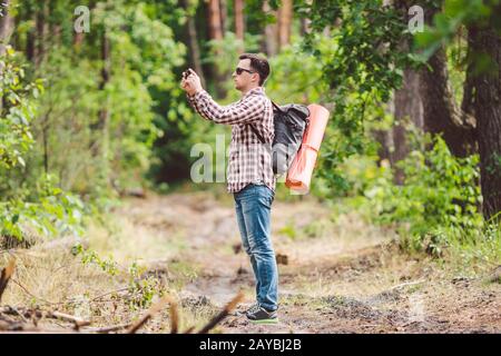 Man hiker taking photo smart phone in forest. Attractive Traveler Making Photo With Mobile Phone. Traveler hiker man with backpa Stock Photo