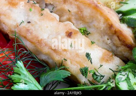 Fried fish with potatoes, vegetables and greens close-up. Stock Photo