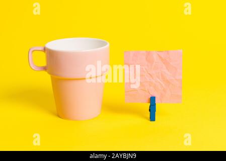 Salmon cup and a empty note paper pinned in a blue clothespin. Square rectangle shaped colored reminder in a yellow background. Stock Photo
