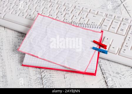 Squared paper notebook with a rectangle shaped empty note above pinned by two clothespins on the sheet. White keyboard under a c Stock Photo