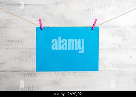 Rectangle shaped note colored paper clipped in a clothesline by clothespin in a white wooden background. Square empty reminder a Stock Photo