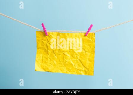 Rectangle shaped note colored paper clipped in a clothesline by clothespin in a white wooden background. Square empty reminder a Stock Photo