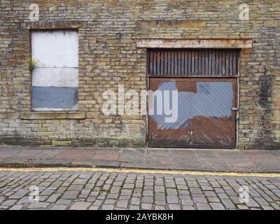 front view of an old abandoned derelict industrial property on an empty street with boarded up window and dilapidated brick wall Stock Photo