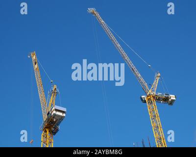 two tall yellow tower cranes working on a construction site against a blue sky Stock Photo