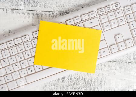 Rectangle shaped note colored paper in a keyboard and a white wooden background. Square empty reminder and office equipments sup Stock Photo