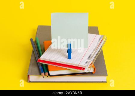 Books, pencils and an empty rectangle square shaped reminder above a blank opened notebook held by a blue clothespin. Office sup Stock Photo