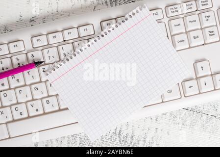 Rectangle shaped note colored paper in a keyboard and a white wooden background. Square empty reminder and office equipments sup Stock Photo