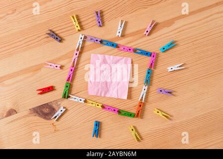 Colored clothespin placed in a square shape and pointing to a empty rectangle reminder note in the centre of a wooden floor. Woo Stock Photo