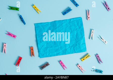 Colorful clothespin spread around a rectangle square shaped colored paper in a light blue background. Note reminder in a blank s Stock Photo