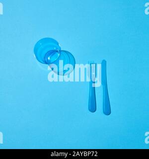 Plastic glass, fork and knife with shadows on a blue table. Stock Photo