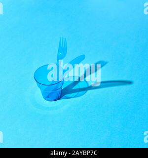 Plastic transparent glass with fork and knife with shadows on surface. Stock Photo