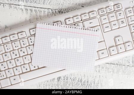 Rectangle shaped note colored paper in a keyboard and a white wooden background. Square empty reminder and office equipments sup Stock Photo