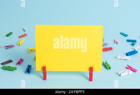 Colorful clothespin and rectangle square shaped colored paper in a blue background. Red clip hanging a note reminder in a blank Stock Photo