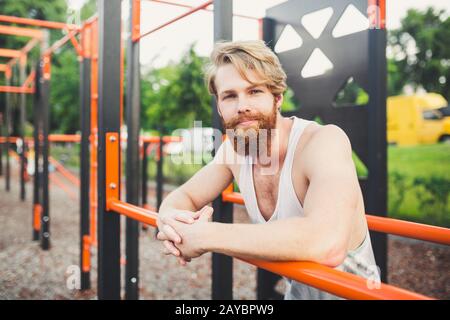 Portrait young bearded man standing on public sports ground and training on parallel bars. Handsome workout athlete. Portrait sp Stock Photo