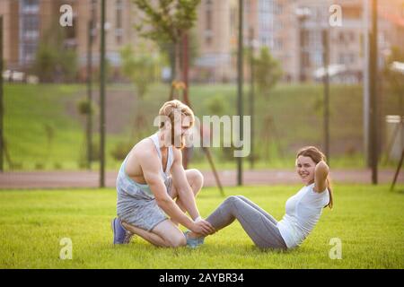 Sit ups fitness couple exercising sit up outside in grass. Fit people working out cross training. Woman doing abdominal crunches Stock Photo