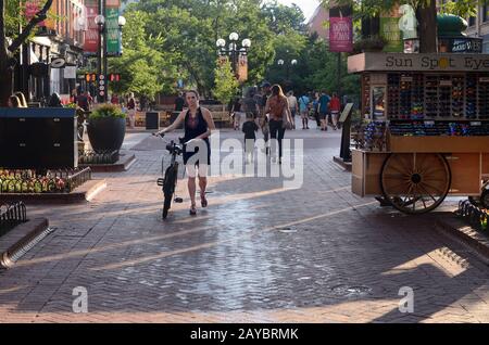 A woman walks her bike on Pearl Street Mall in Boulder, CO. Bike riding is not allowed on the mall. Stock Photo