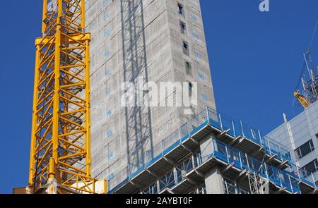 close up of a large urban construction site with a yellow tower crane casting a shadow on a large concrete building and safety f Stock Photo