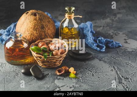 Natural macadamia and coconut oil in aglass bottles with macadamia nuts on wooden board Stock Photo