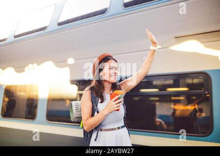 backpack traveler woman waving hand at train station platform summer holiday traveling concept. Female tourist greeting and enjo Stock Photo