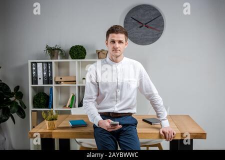 Attractive young businessman using a cell phone. Cheerful Businessman With Smartphone Standing In An Office. Portrait of man in Stock Photo