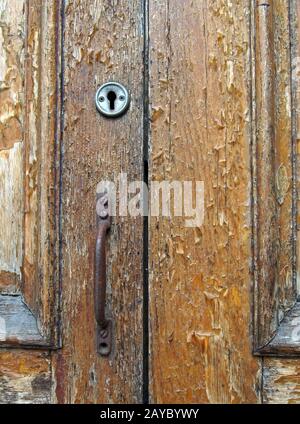 close up of an old brown varnished peeling wooden door with keyhole and rusty handle Stock Photo