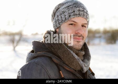 Young man smiling in a winter scene landscape. Christmas and winter wear concept. Stock Photo