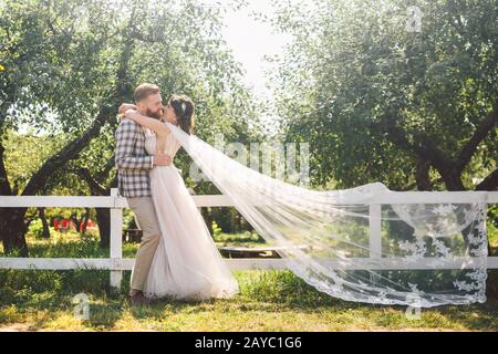 Caucasian couple in love bride and groom standing in embrace near wooden white, rural fence in park an apple orchard. theme is w Stock Photo