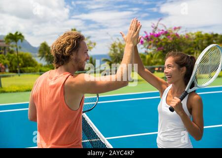 Fitness sport tennis couple giving high five energetic after fun mixed double game. Tennis players friends having fun doing fit sport at hotel ,summer travel vacation. Asian woman, Caucasian man. Stock Photo