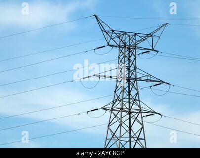 tall metal electricity pylon with multiple cables against a blue cloudy sky Stock Photo