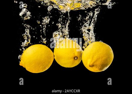 Fresh yellow lemons in water splash on black background with lots of air bubbles. Stock Photo
