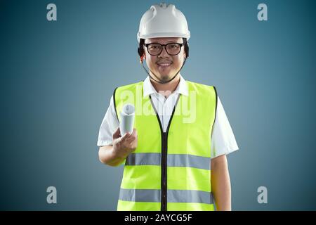 Portrait of confident asian young engineer wearing protective hard hat and holding paper blueprint . Stock Photo