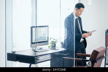 Asian businessman in the office standing and using a digital tablet to work . Stock Photo