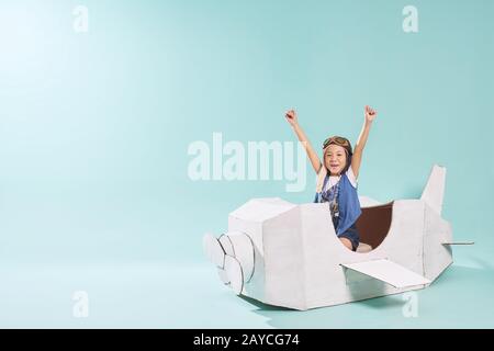 Little asian girl is happy sitting on a hand made cardboard paper plane . Isolated on mint green background . Stock Photo