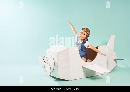 Little cute girl playing with a cardboard airplane. White retro style cardboard airplane on mint green background . Childhood dr Stock Photo