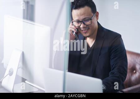Young asian businessman using handphone and computer working Stock Photo