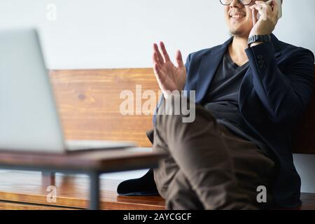 Businessman sit on wooden chair using smartphone in front of the laptop. Stock Photo