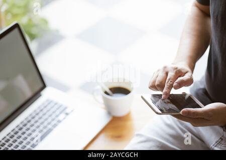 Smartphone in young man hand with blur laptop and coffee background Stock Photo