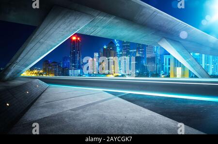 Empty asphalt road under the bridge during the night with beautiful city skyline background . Stock Photo