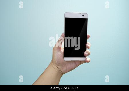 Hand holding mobile smart phone with blank screen. Isolated on light blue background. Stock Photo