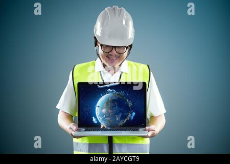 Young engineer in safety helmet and using laptop with virtual reality earth to show client something. Stock Photo