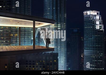 Businessman in an modern sky office by night with beautiful city skyline view . Stock Photo