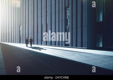 Two young businessmen walking in the streets of facade with metal and stripes design construction in modern building . Stock Photo