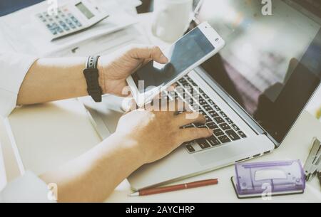 businessman hand using smart phone and keying the data to laptop Stock Photo