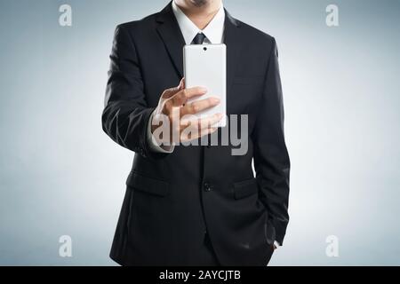 Smart businessman in black suit standing while make a selfie by hand phone on grey background . Stock Photo