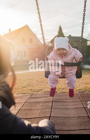 Adorable baby girl with big beautiful eyes and a beanie having fun on a swing Stock Photo