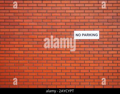 a white sign saying no parking on a red brick wall Stock Photo