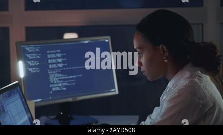 Close up of african american woman working on computer in electronics laboratory. Doing Development of Software and Hardware. She wearing a lab coat. Side view Stock Photo