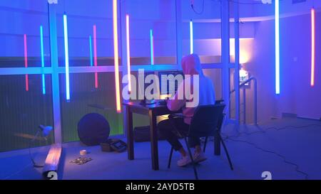 Hacker working place: hacker working in a room with colored neon lights. He writing hacker program. Hooded Hacker Breaks into Government Data Servers. Stock Photo