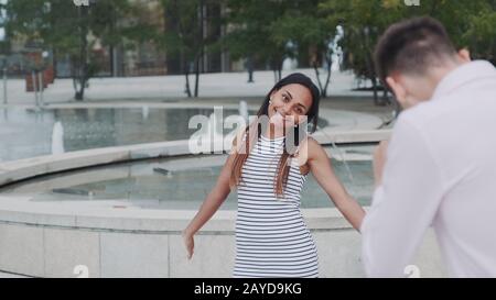Young man taking photo of his beautiful black girlfriend in city center. Fountains are in the background. Stock Photo