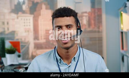 Close-up shot of mixed-race customer service operator talking to client in call center with skyscrapers in the background. Stock Photo
